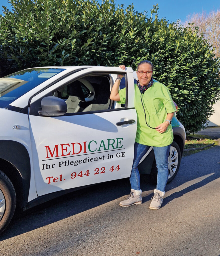 Eine Mitarbeiterin des Medicare Pflegedienstes Gelsenkirchen steht an ihrem Fahrzeug, mit dem sie sich täglich auf den Weg zu ihren Patientinnen und Patienten macht.