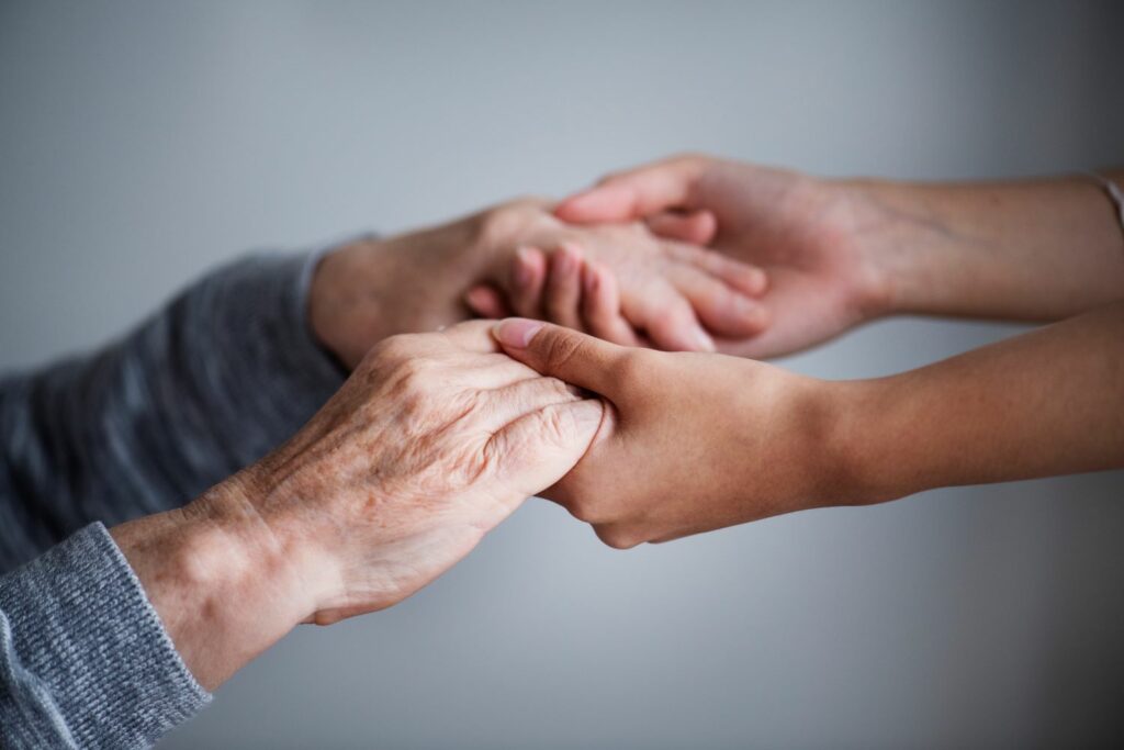 Eine Pflegekraft hält unterstützend die Hände einer älteren Person.